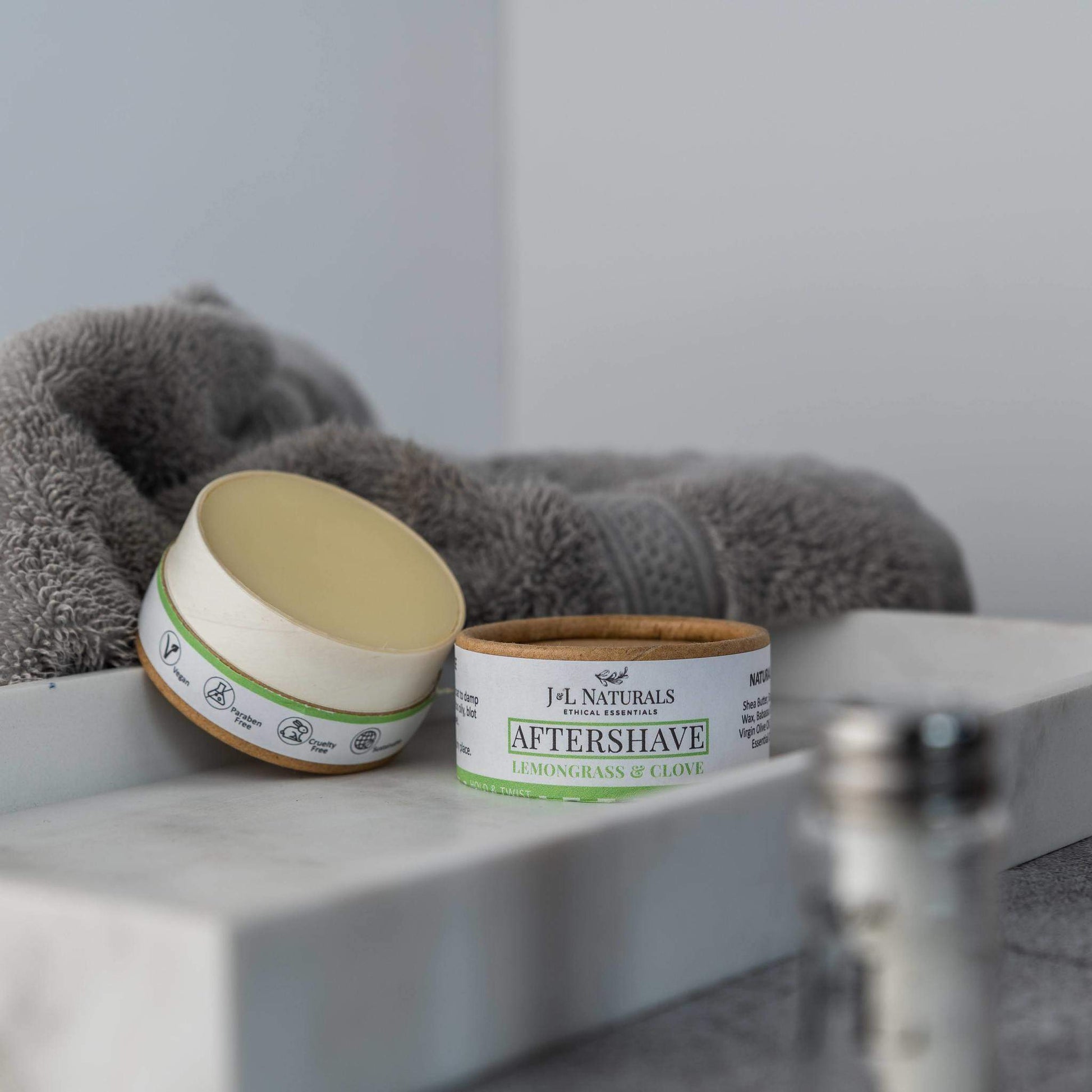 Two jars of aftershave on a bathroom shelf with a towel in the background