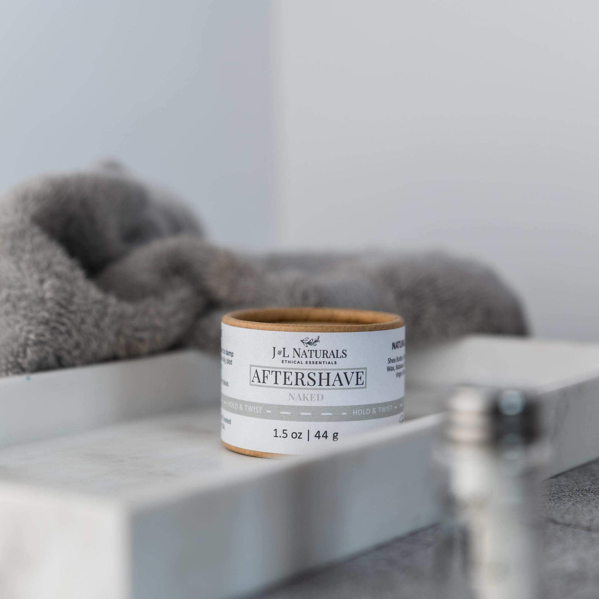 J.L Naturals aftershave jar on a shelf with a gray towel in the background