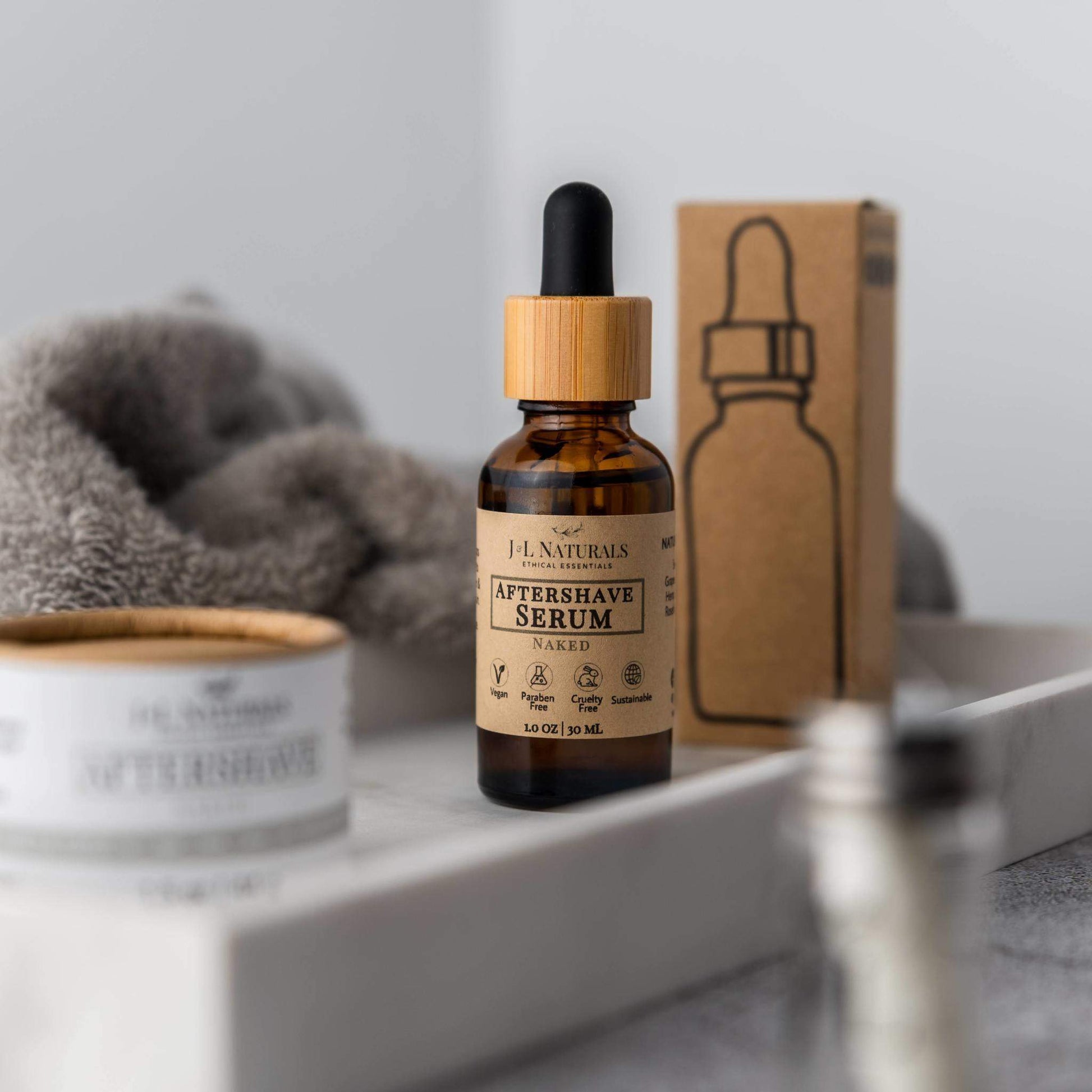 Aftershave serum bottle with wooden dropper on a bathroom counter with a box in the background.