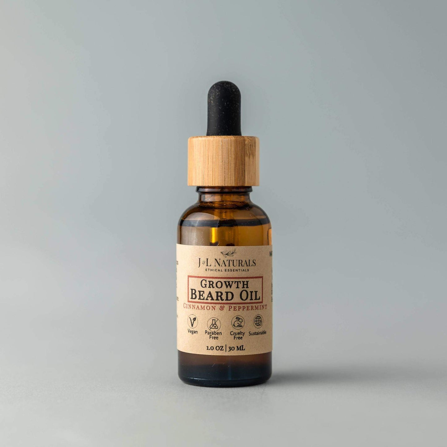 Bottle of J.L. Naturals Growth Beard Oil with a wooden dropper on a gray background