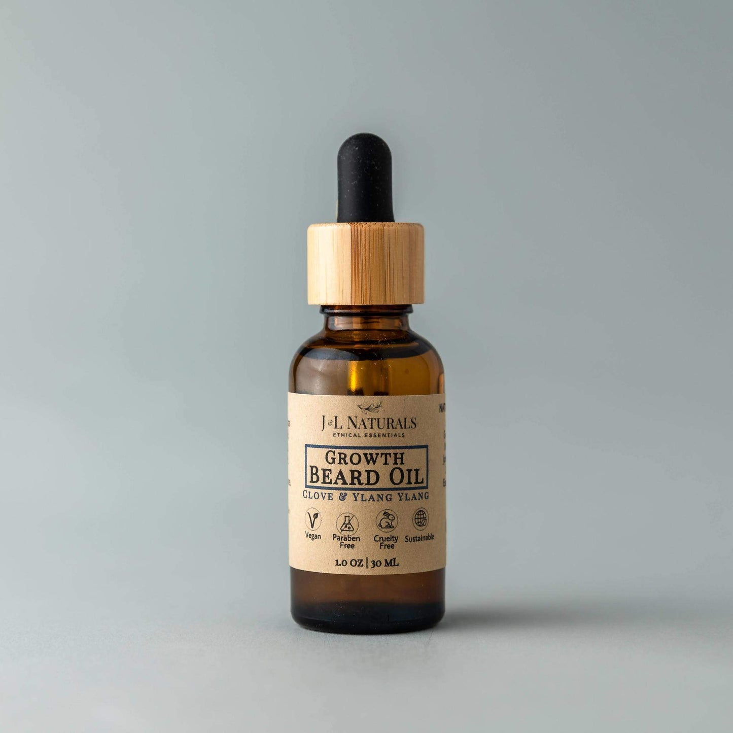 Bottle of J.L Naturals beard oil with a wooden dropper on a gray background