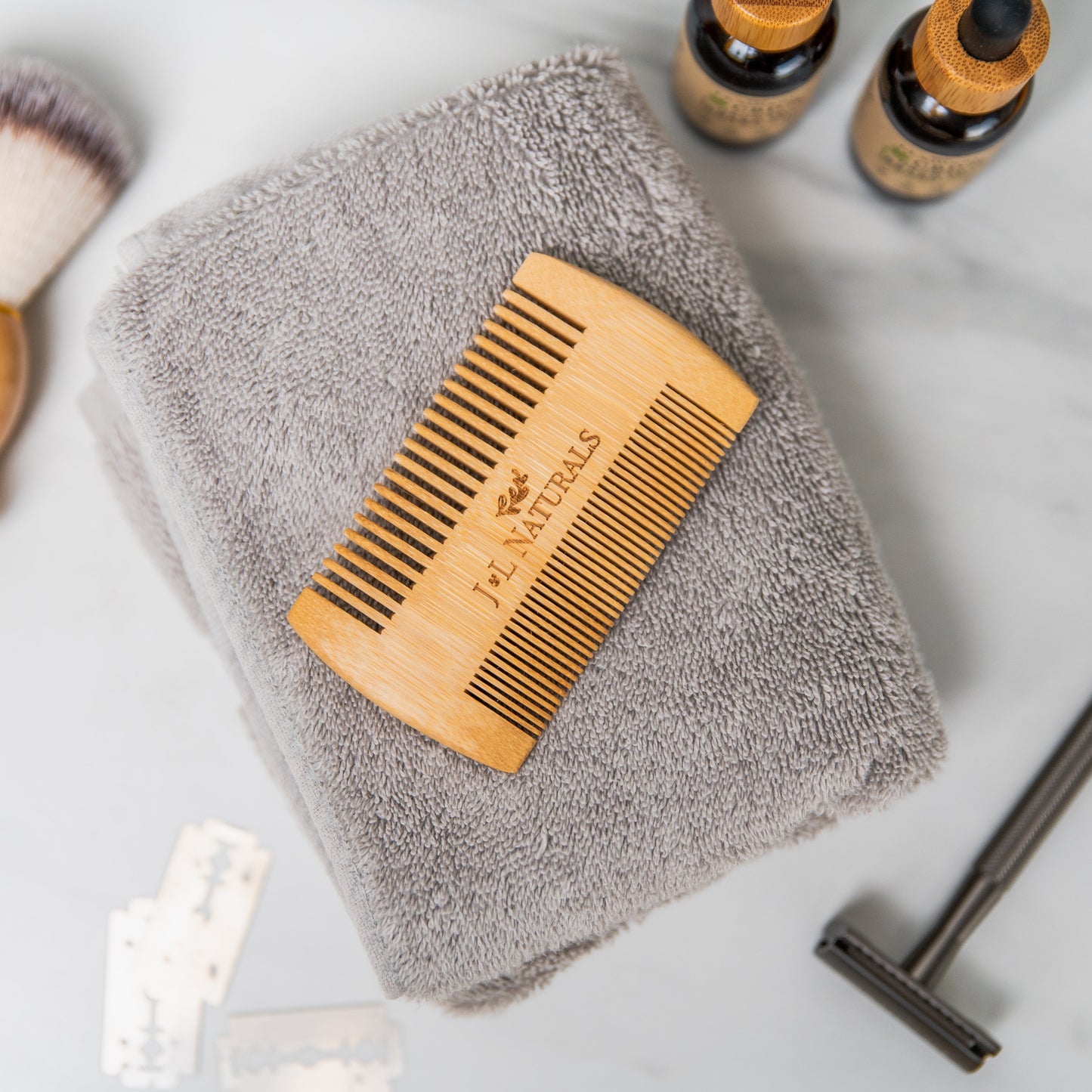 Wooden comb on a gray towel with bottles and a razor in the background