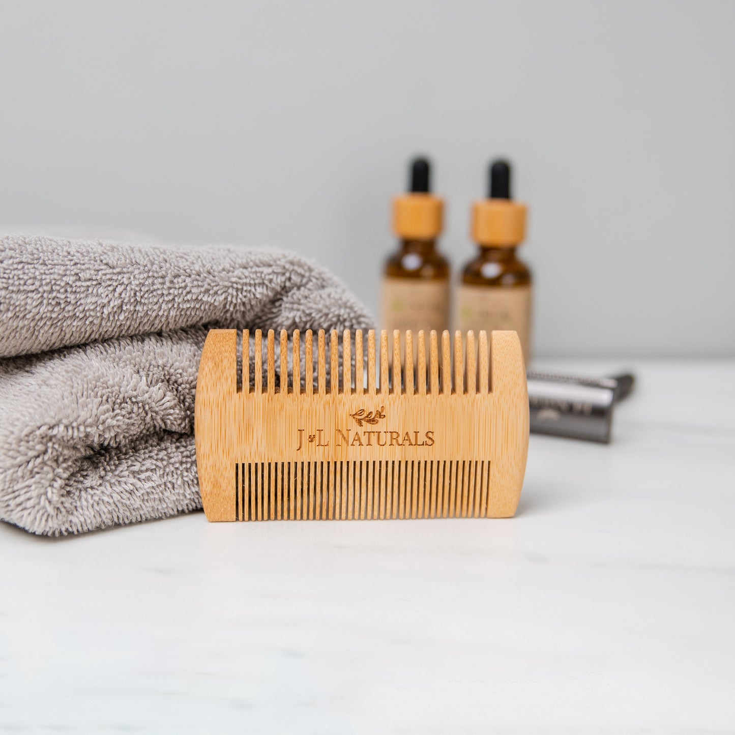 Bamboo comb with 'J&L Naturals' branding on a light surface with a towel and bottles in the background.